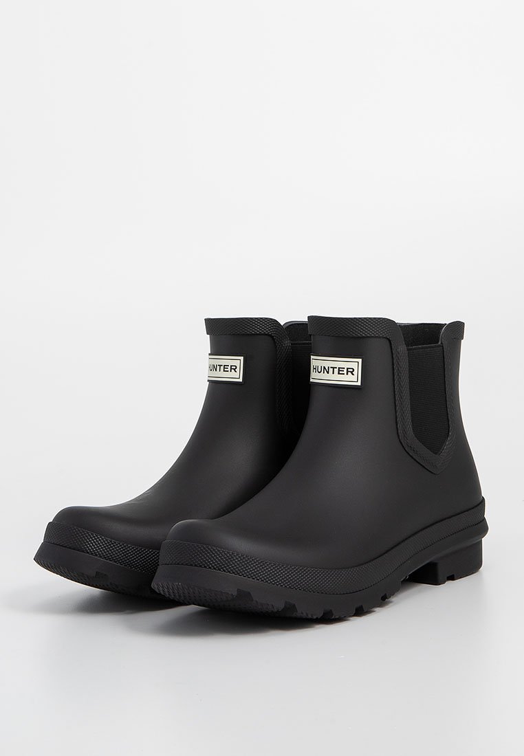 Par de botas de lluvia negras de altura hasta el tobillo de Hunter con suelas texturizadas y paneles laterales elásticos sobre un fondo blanco.