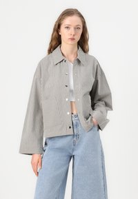 Stripet avkortet jakke i grått og hvitt, med krage, knappelukking og store ermer. Kombinert med høyt liv denimjeans.