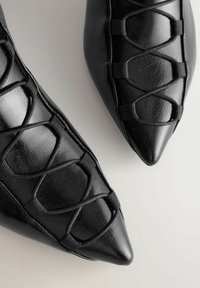 Mustat kärjelliset ballerinat, jotka on valmistettu teksturoidusta nahasta. Ominaisuudet ristiin kulkevasta elastisesta yksityiskohdasta ja sileästä viimeistelystä, tyylikkäällä designilla.