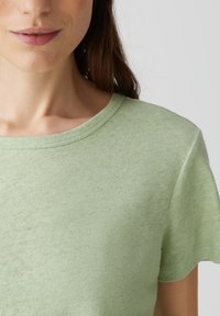 Maglietta a maniche corte di colore verde chiaro, realizzata in un tessuto strutturato con scollo rotondo e sottili variazioni di colore per un look casual.