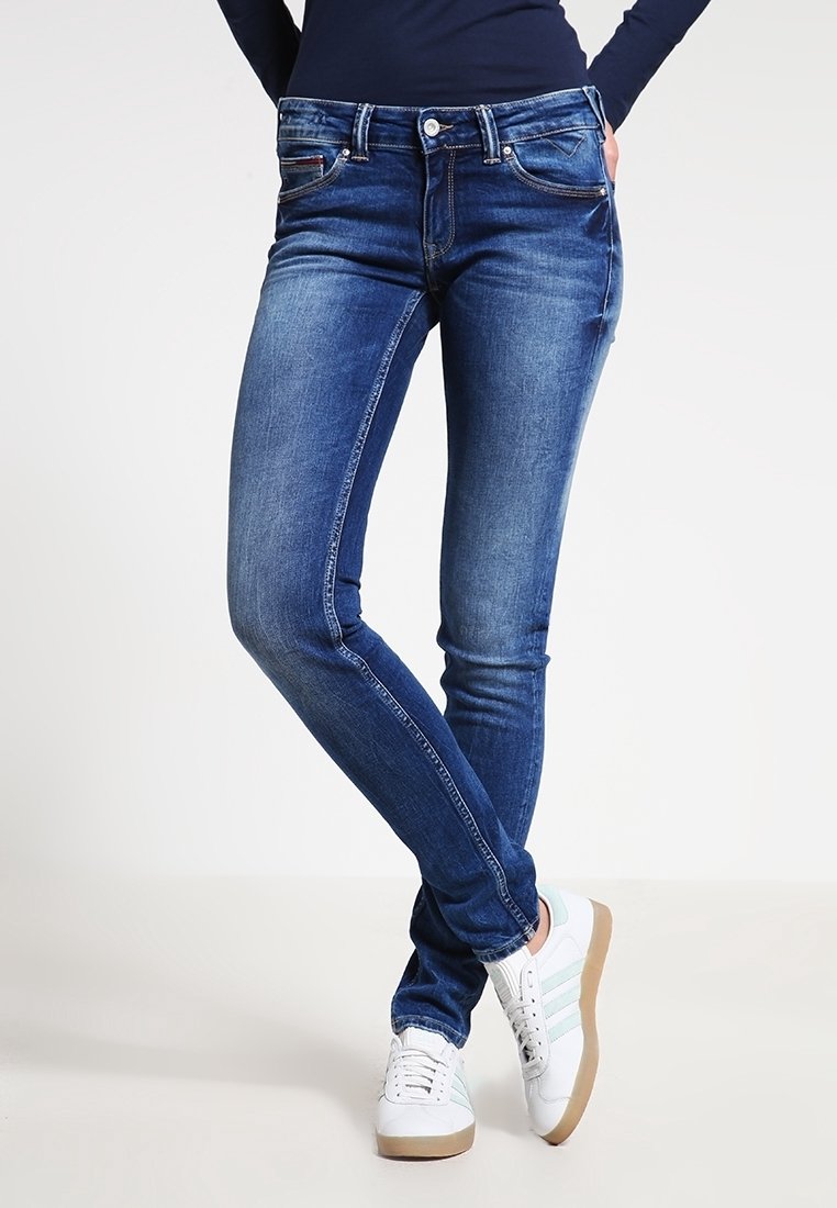 Slim-fit blå denimjeans med en urtvättad look, med fem fickor, bälteshällor och subtila sömnadsdetaljer, kombinerat med vita sneakers.
