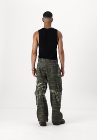 Svart ärmlös topp och byxor i kamouflage-mönster med sidfickor och en lös passform, sedd bakifrån mot en vit bakgrund.