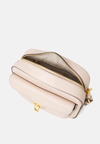 Svetle béžová kožená crossbody taška s texturovaným povrchem, zlatými doplňky a zipovým uzávěrem. Obsahuje malou přední kapsu.