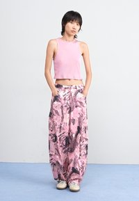 Rózsaszín világos crop top, laza szabású, mintás rózsaszín nadrággal, absztrakt fekete mintákkal. A megjelenést sportcipők egészítik ki.
