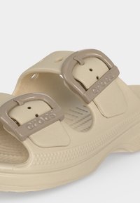 Sandale Crocs beige avec deux brides ajustables avec des boucles en plastique arrondies gravées du logo Crocs.