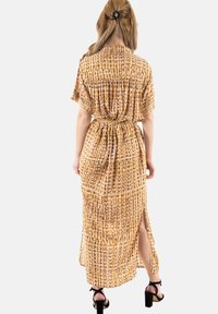 Vestido de tela color amarillo mostaza con patrones morados y blancos, mangas cortas, cintura ajustada y aberturas laterales, de longitud hasta los tobillos y con un corte holgado.