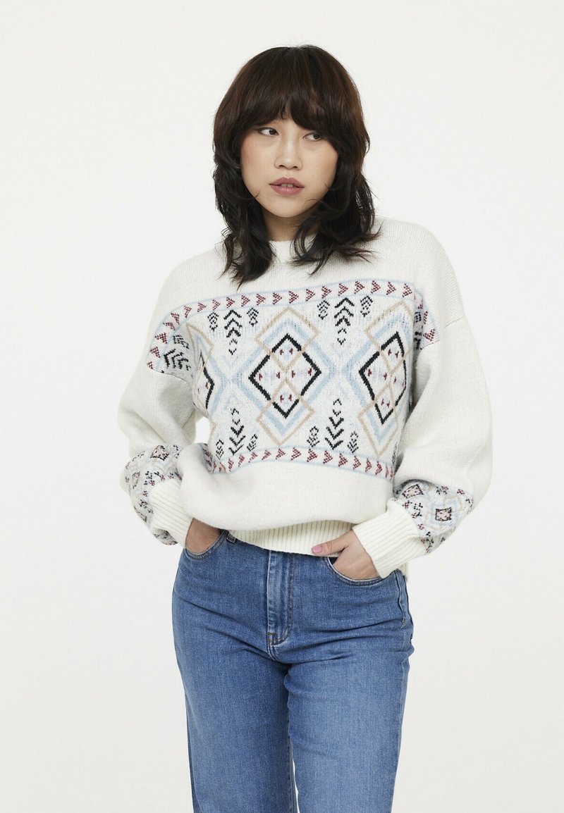 Pull blanc en tricot avec des motifs géométriques dans un doux bleu, rouge et noir. Dispose de poignets côtelés et d'une coupe décontractée. Associé à un jean bleu.