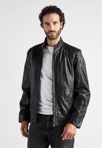 Zwart leren jack met staande kraag, ritssluiting aan de voorkant en twee zijzakken. Beschikt over gestructureerde schouderpanelen en een gladde afwerking.