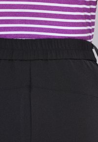 Elastische tailleband van zwarte broeken gecombineerd met een paarse en witte gestreepte top. De focus ligt op het taillegebied en de stoftextuur.