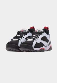 Ζεύγος αθλητικών παπουτσιών σε μαύρο, λευκό και κόκκινο χρώμα με μαύρα κορδόνια, πάνελ από δίχτυ, κόκκινες γλωττίδες στη φτέρνα και λογότυπα στη λευκή γλώσσα, στραμμένα μπροστά σε λευκό φόντο.