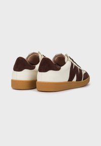 Zapatillas blancas de cuero con acentos de ante marrón oscuro, tacón redondeado y suela de goma beige. Presentan cordones marrones y un diseño texturizado.