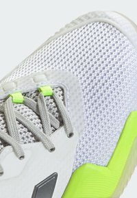 Zapatilla deportiva ligera con parte superior de malla en blanco con acentos grises, detalles en verde lima y suela de goma texturizada para mayor agarre.