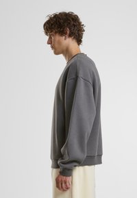 Felpa grigia con maniche lunghe, collo rotondo e polsini a coste. Realizzata in tessuto morbido, presenta una vestibilità comoda e un design minimalista.