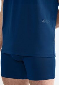 Maglietta sportiva blu navy con slip coordinati; tessuto morbido, design aderente, texture liscia, con il marchio SLG vicino all'orlo della maglietta.