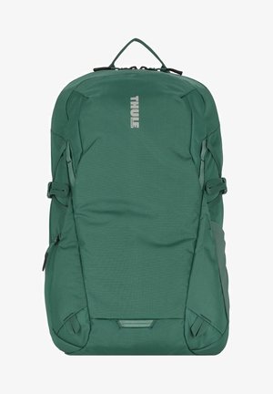 Sac à dos Thule en vert foncé, fabriqué en tissu durable. Dispose d'une poignée supérieure, de poches latérales et de sangles réglables. Texture lisse avec un design minimaliste.