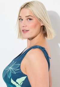 Tyrkysový plavecký top s květinovým potiskem v světlé zelené barvě. Obsahuje nastavitelné ramínka a přiléhavý střih. Hladká, pružná textilie.