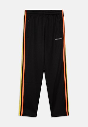 Pantaloni sportivi neri con strisce laterali arancioni e gialle, cintura con cordino e tasche con zip. Logo Adidas sull'anca.