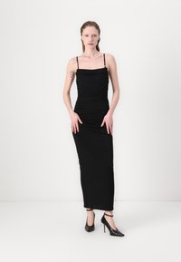 Černé, přiléhavé šaty s tenkými ramínky a nahrnutou strukturou, sahající až na zem. Nošeny s černými vysokými podpatky. Jednoduchý, elegantní design.