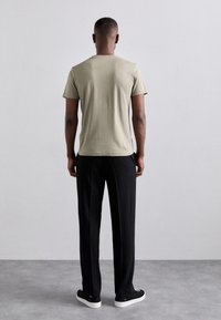 Zielona oliwkowa koszulka z krótkim rękawem o prostym wzorze, w połączeniu z luźnymi czarnymi spodniami i czarnymi sneakersami. Prosty i stonowany styl.