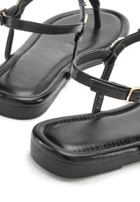 Črne ravne sandale z gladkim usnjem, tankimi naramnicami in zlatimi detajli. Podplat je raven s rahlim robom.