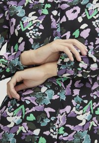Floral-patterned shirt featuring shades of purple, green, and black with button closure and cuffed sleeves. Smooth fabric texture.