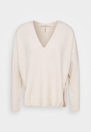 Pull crème à col en V manches longues avec poignets et ourlet côtelés, comportant des fentes latérales avec détails zippés.