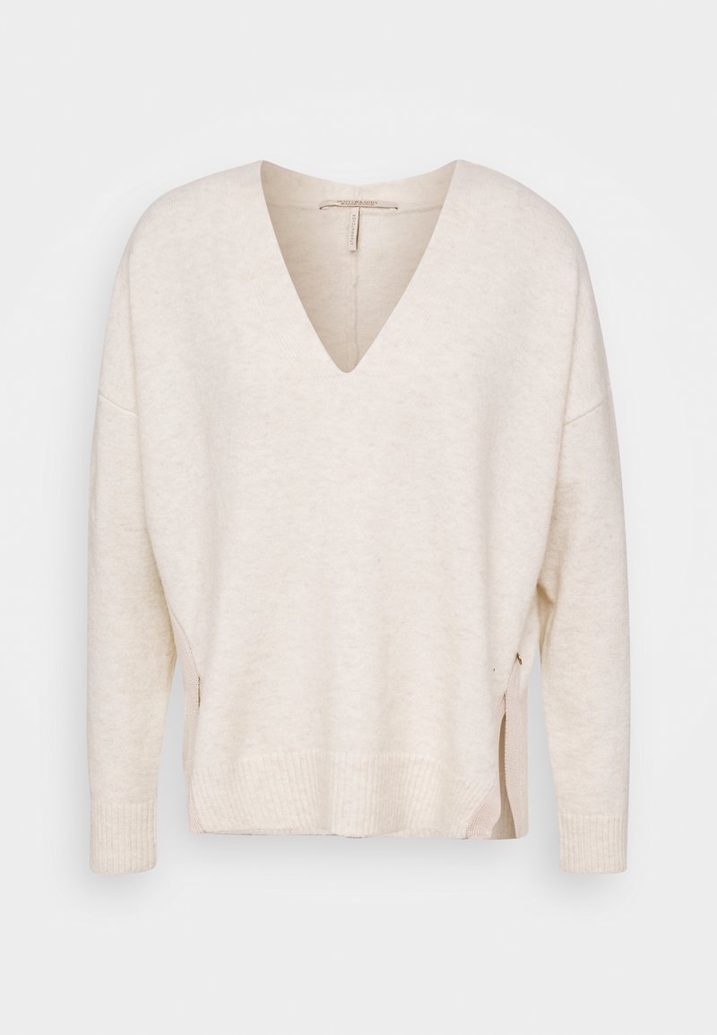 Pull crème à col en V manches longues avec poignets et ourlet côtelés, comportant des fentes latérales avec détails zippés.