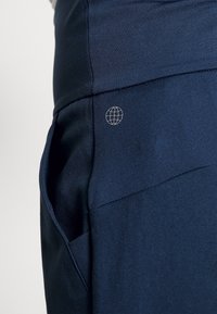 Marineblå idrottsbyxor med en mjuk textur, strukturerad passform och en liten jordglob-logotyp på sidofickan.