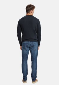 Suéter de punto azul oscuro con mangas largas, combinado con jeans de mezclilla azul claro que tienen bolsillos traseros. Calzado casual completa el look.