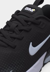 Κοντινό πλάνο ενός μαύρου αθλητικού παπουτσιού με μαύρα κορδόνια, λευκό λογότυπο Nike στη πλευρά, υφασμένη επάνω επιφάνεια και λογότυπο "AM" στη γλώσσα.