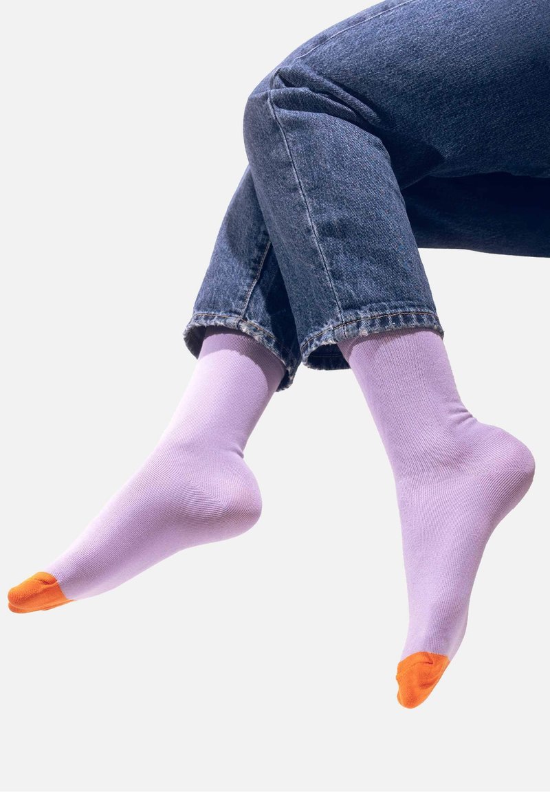 Jasnofioletowe bawełniane skarpetki z pomarańczowymi akcentami na palcach, o gładkiej teksturze i prążkowanym mankiecie, noszone z dżinsami z podwiniętymi nogawkami.