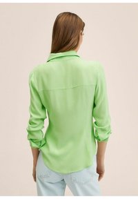 Lange mouw shirt van helder groene stof, met een klassieke kraag, knoopmanchetten en een ronde zoom. Achteraan is er minimale stiksels zichtbaar.