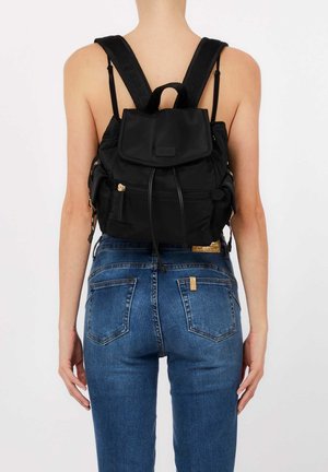 Donna che indossa jeans blu e un piccolo zaino nero con molte tasche con cerniera, vista da dietro.