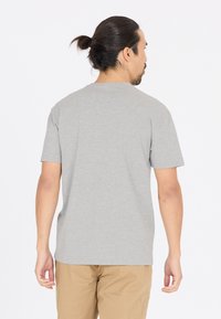 Harmaat puuvillaiset t-paidat, joissa on lyhyet hihat ja ympyräkaulus, esitetty takaa, yhdistettynä vaaleanruskeisiin housuihin. Silkkinen pinta, yksinkertainen muotoilu.