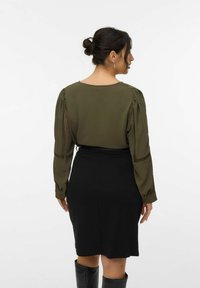 Oliven grøn top med puffede ærmer og mesh detaljer, parret med en tætsiddende sort nederdel. Sættet har en glat tekstur og et afslappet design.