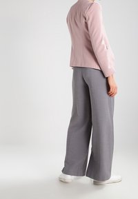 Veste cintrée rose clair au design structuré, associée à un pantalon ample gris à jambes larges. La tenue est complétée par des baskets blanches.