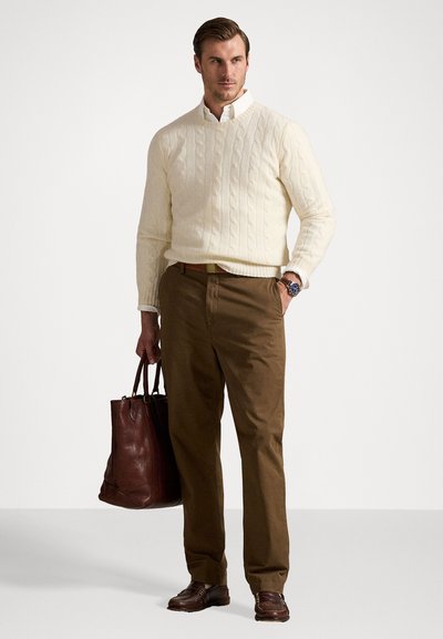 Cream cable-knit sweater, white collared shirt, brown chinos, brown leather shoes, and dark brown leather tote bag. Neat, tailored look.