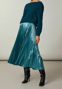 Mintgrön stickad tröja i kombination med en glänsande mintgrön plisserad kjol och svarta knähöga stövlar. Kjolen har vertikala plisseringar och en luftig design.