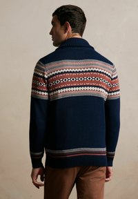 Granatowy sweter z prążkowanym kołnierzem i wzorzystym przodem w kolorze burgundowym, kremowym i granatowym. Posiada dopasowany krój oraz długie rękawy z prążkowanymi mankietami.