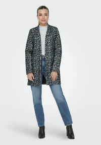 Manteau en imprimé léopard avec un motif noir et gris, à manches longues, à ouverture devant, associé à un jean bleu clair et des bottines noires.
