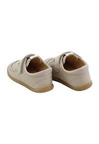 Zapatos de piel beige con una correa de Velcro, forma redondeada, detalles de costura en contraste y una suela de goma con un agarre texturizado.