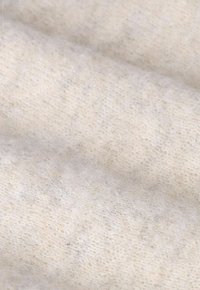 Tissu en tricot de couleur crème, doux et duveteux, avec une texture subtile, présentant des fils délicats et un motif uniforme.