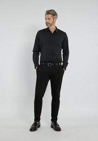 Czarna koszula z guzikami i dopasowane spodnie, obie z gładkiego materiału. Noszone z czarnym paskiem i butami, wyróżniającymi się eleganckim, minimalistycznym stylem.