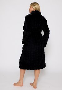 Zwarte pluche badjas met een gestructureerd, golvend ontwerp. Het heeft een sjawlcollar, lange mouwen en een strik in de taille. Zacht, luxueus stof.