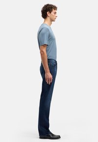 Gładki niebieski t-shirt w połączeniu z ciemnoniebieskimi dżinsami. Dżinsy mają prosty krój nogawek oraz subtelne przeszycia. Całość uzupełniają czarne buty.