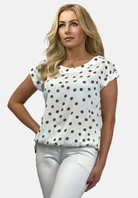 Biała bluzka z krótkim rękawem w czarne kropki, o luźnym kroju i okrągłym dekolcie. Noszona z białymi spodniami. Gładki, lekki materiał.