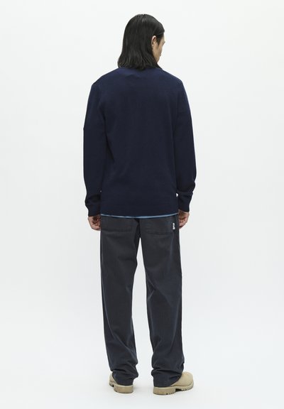 Navy sweater with long sleeves, ribbed cuffs, and hem, paired with dark gray pants featuring a patch pocket and logo tag. Light background.