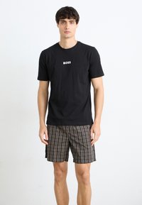 Schwarzes Baumwoll-T-Shirt mit weißem "BOSS"-Logo, kombiniert mit braunem kariertem Shorts mit mehreren Farben und einem lockeren Schnitt.