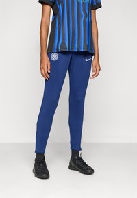 Blå Nike treningsbokser med slim passform, med brodert logo. Sammen med en svart og blå stripete genser. Svart treningssko.
