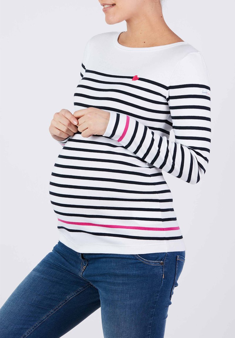 Gestreiftes Umstandstop in Weiß mit schwarzen Streifen, verziert mit einem rosa Herzakzent und einem rosa Streifen am Saum. Weiches, elastisches Material.